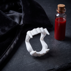 Vampire fangs with a black cape collar and fake blood vial styled on a dark surface